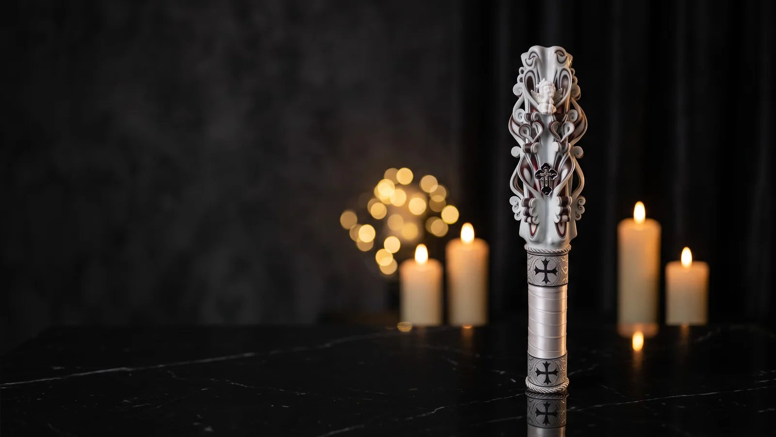 Lumânare ceremonială SACRIEL, sculptată manual în alb, argintiu și negru, cu cruce în relief, așezată pe marmură neagră în lumina caldă a lumânărilor