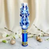 Lumânare ceremonială sculptată manual, albă cu albastru regal și auriu, cu motive de cruce, fotografiată pe fundal elegant luminos