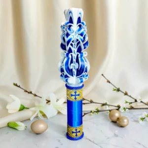 Lumânare ceremonială sculptată manual, albă cu albastru regal și auriu, cu motive de cruce, fotografiată pe fundal elegant luminos